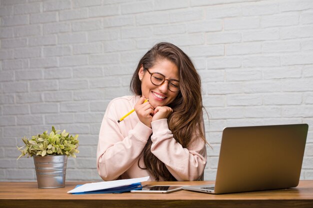 Retrato de joven estudiante mujer latina sentada en su escritorio muy feliz y emocionada