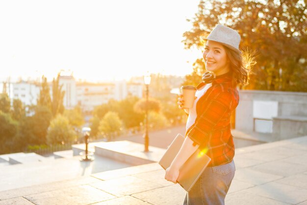 Retrato de una joven estudiante en sun flare. Niña sonriente sosteniendo un portátil en la ubicación de la ciudad