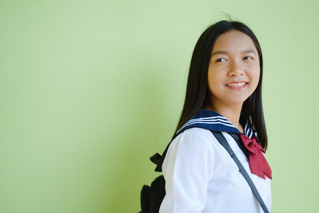 Retrato de joven estudiante en uniforme escolar y mochila en pared verde. Asiático chica adolescente