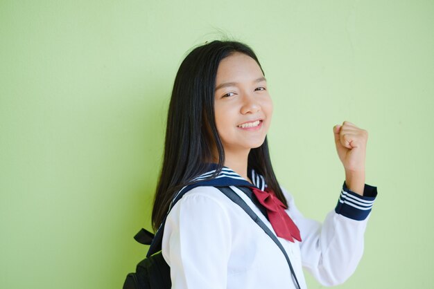 Retrato de joven estudiante en uniforme escolar y mochila en pared verde. Asiático chica adolescente