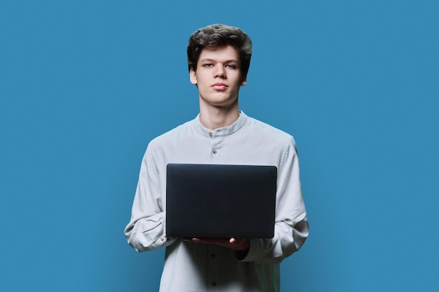 Retrato de un joven estudiante universitario usando una computadora portátil sobre un fondo azul