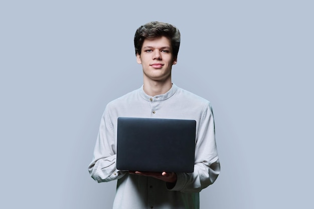 Retrato de un joven estudiante universitario usando una computadora portátil sobre un fondo gris