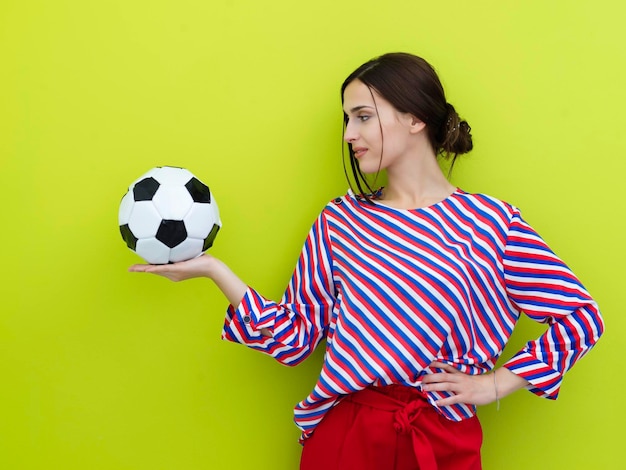 Retrato de una joven europea sosteniendo un balón de fútbol en la palma de su mano. Niña feliz, fanática del fútbol o jugadora aislada de fondo verde. Deporte, jugar al fútbol, salud, concepto de estilo de vida saludable