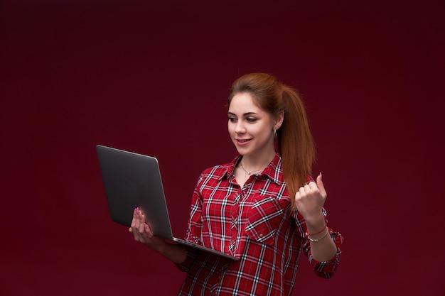 Retrato de una joven excitada pelirroja en una camisa marcada con laptop