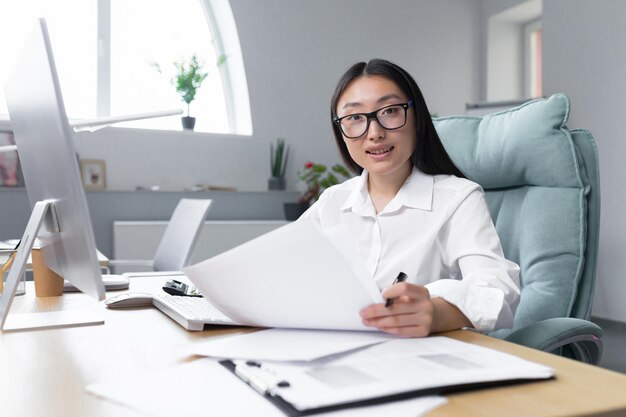 Retrato de una joven y exitosa mujer de negocios financiera asiática que trabaja en el cargo con documentos sonriendo