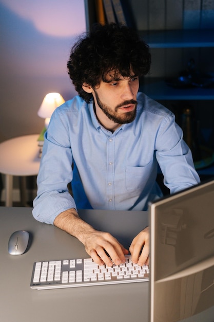 Retrato de un joven exitoso escribiendo un mensaje en línea sentado en la mesa y mirando a la cámara