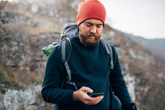 Retrato de un joven explorador barbudo caminando por las montañas usando un teléfono móvil para la aplicación GPS Hombre viajero enviando mensajes de texto y navegando en Internet a través de su teléfono inteligente después de caminar en la montaña