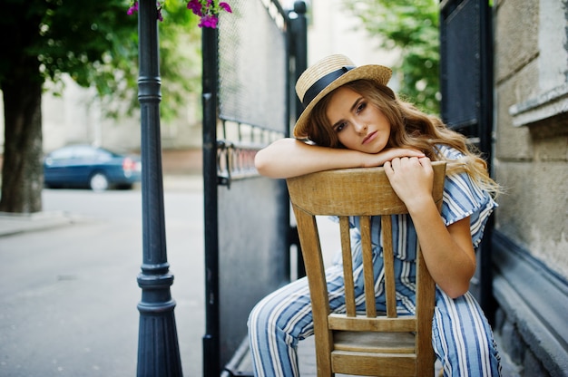Retrato de una joven fabulosa en general a rayas y sombrero sentado y posando en la silla al aire libre.