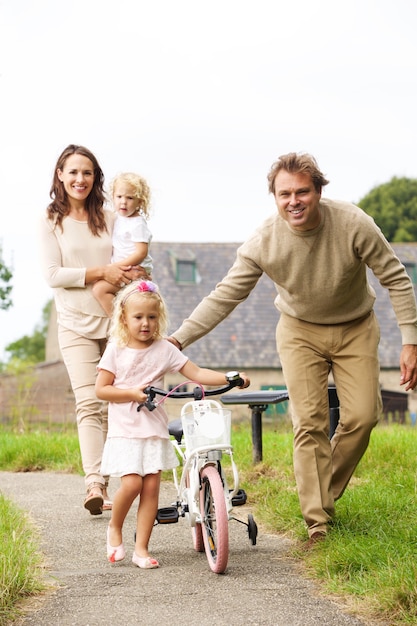 Retrato de joven familia feliz de cuatro con una pequeña bicicleta caminando en el parque