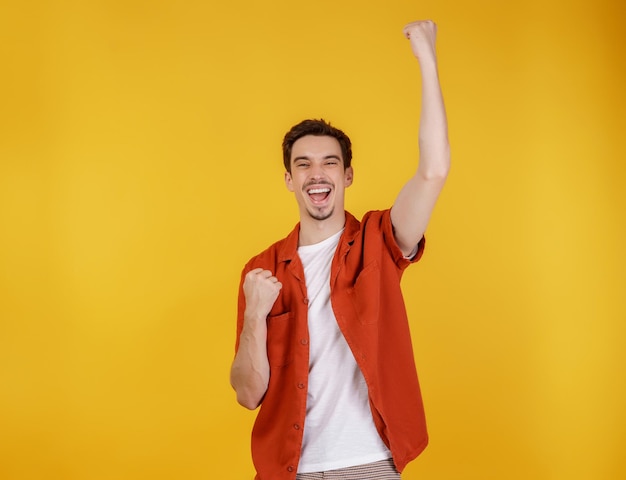 Retrato de un joven feliz y alegre de pie haciendo un gesto de ganador apretando los puños manteniéndose aislado en un estudio de fondo de pared de color amarillo