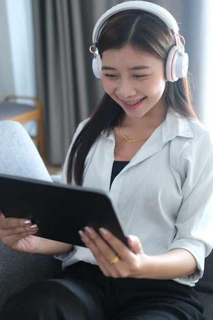 Retrato de una joven feliz en auriculares disfrutando con medios de entretenimiento en línea con tableta el fin de semana en casa.