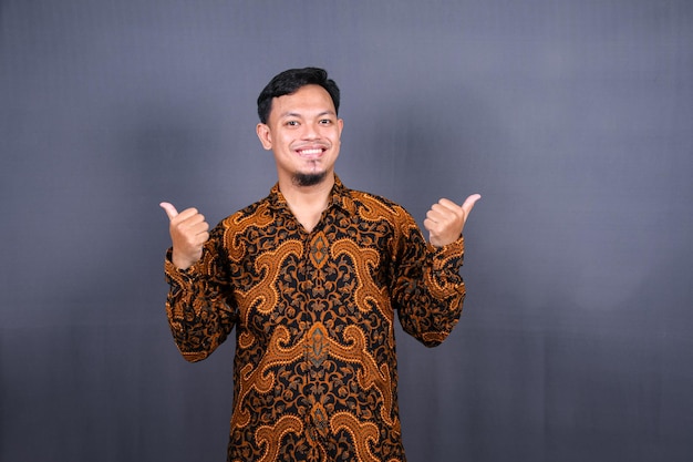 Retrato de un joven feliz en batik indonesia señalando con el dedo el espacio de la copia. aislado