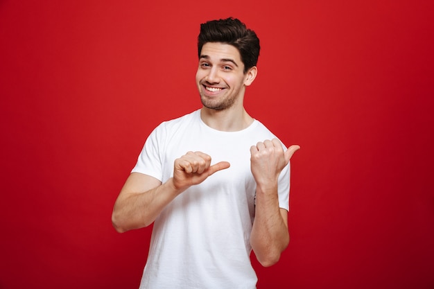 Retrato de un joven feliz en camiseta blanca apuntando