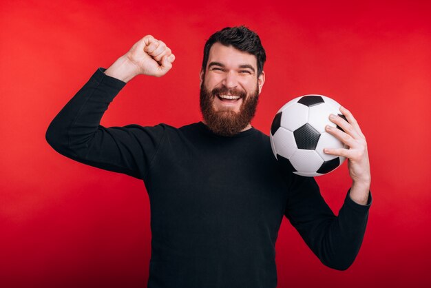 Retrato de joven feliz celebrando la victoria y sosteniendo el balón de fútbol