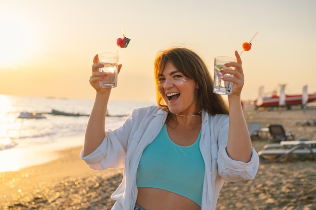 Retrato de una joven feliz con un cóctel en la mano sobre un fondo de mar hermoso Chica divirtiéndose en vacaciones de verano Libertad y felicidad