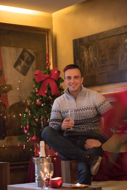 Retrato de un joven feliz con una copa de champán celebrando las vacaciones de invierno en casa bellamente decorada para Navidad