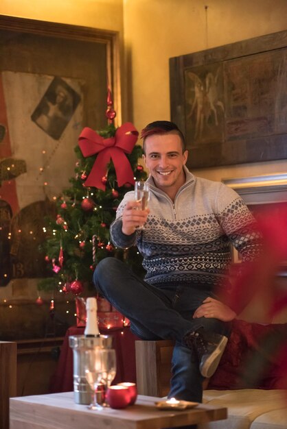 Retrato de un joven feliz con una copa de champán celebrando las vacaciones de invierno en casa bellamente decorada para Navidad