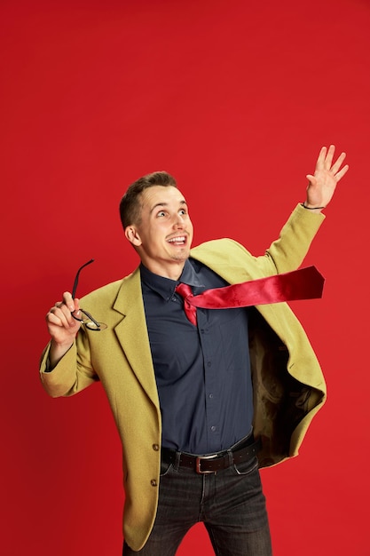 Retrato de un joven feliz con una elegante chaqueta y gafas posando mostrando entusiasmo por el fondo rojo Ganar Concepto de ocupación de emociones de negocios