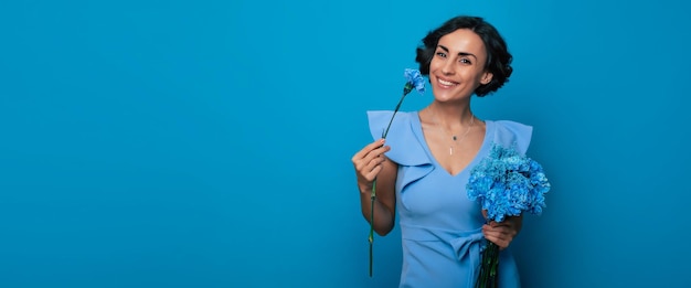 El retrato de una joven feliz y emocionada con un elegante vestido azul posa con un ramo fresco de flores azules. Día de la Madre. Vacaciones de mujeres. Primavera. Derechos de las mujeres