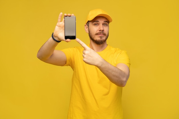 Retrato de un joven feliz emocionado repartidor con gorra amarilla que se encuentran aisladas sobre la pared blanca