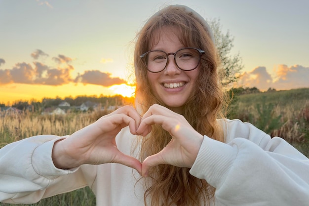 Retrato de una joven feliz con gafas al atardecer sobre un fondo natural, sonríe y mira la cámara