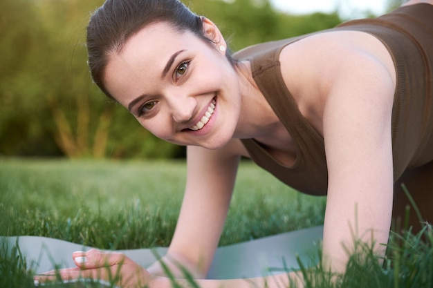 Retrato de una joven feliz haciendo yoga en el parque sobre una alfombra