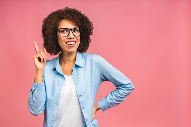 Retrato de una joven y feliz mujer de negocios negra afroamericana señalando con el dedo el espacio de copia aislado sobre fondo rosa