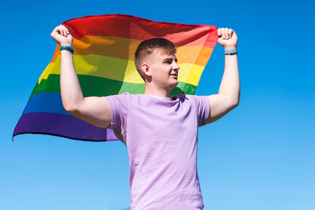 Retrato de joven feliz orgulloso hombre gay guapo está ondeando la bandera gay de color lgbt arco iris en verano