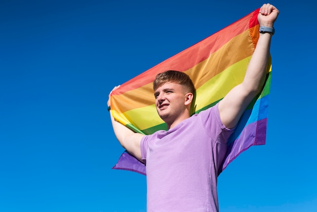 Retrato de joven feliz orgulloso hombre gay guapo está ondeando la bandera gay de color lgbt arco iris en verano
