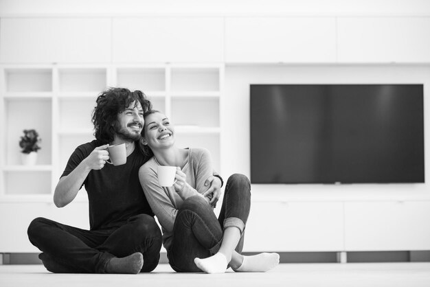 retrato de una joven y feliz pareja sentada en el suelo y tomando café en su nuevo hogar