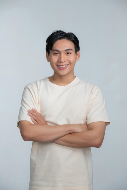 Retrato de un joven feliz posando con los brazos cruzados sobre un fondo blanco.