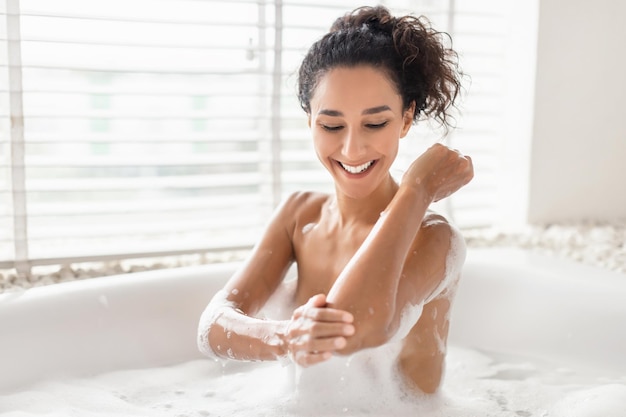 Retrato de una joven feliz relajándose en un baño tibio con espuma tocando su piel suave disfrutando