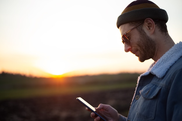 Retrato de joven feliz con smartphone en mano sobre fondo de puesta de sol