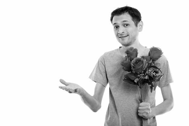 Retrato de joven feliz sonriendo mientras sostiene rosas rojas y mostrando algo listo para el día de San Valentín