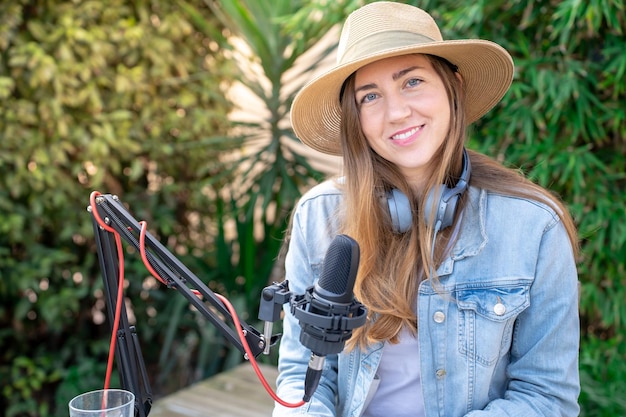 Retrato de una joven feliz y sonriente con auriculares grabando podcast al aire libre en primavera al atardecer