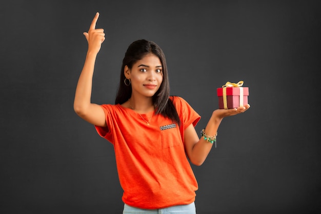 retrato, de, joven, feliz, sonriente, niña, tenencia, caja obsequio, en, un, fondo gris