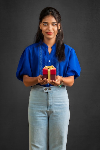 retrato, de, joven, feliz, sonriente, niña, tenencia, caja obsequio, en, un, fondo gris