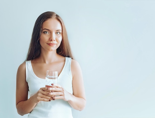 Retrato de una joven feliz y sonriente posando en un estudio aislado con un vaso de agua