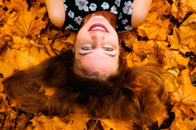 Retrato de joven feliz sonriente, tumbado en hojas de otoño