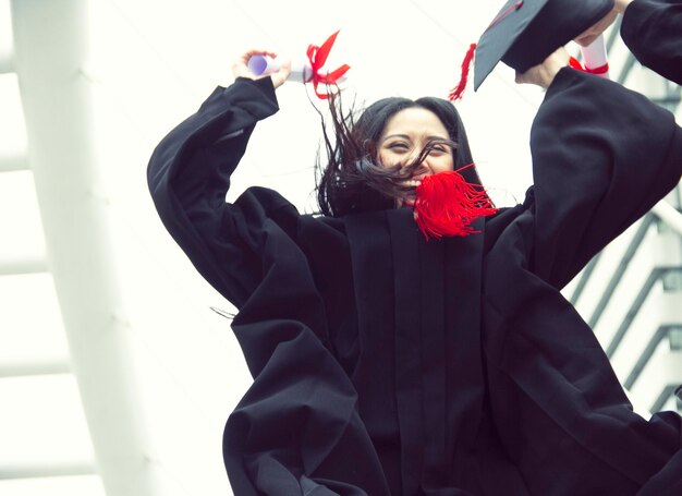 Foto retrato de una joven feliz con una túnica de graduación con certificado y cartón de mortero