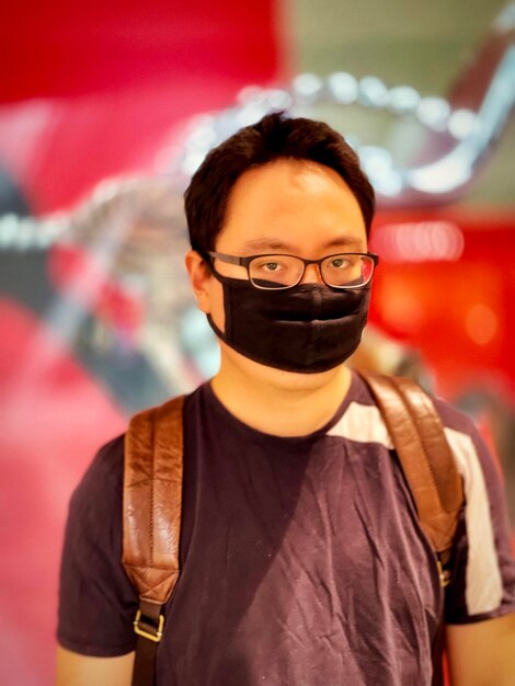 Retrato de un joven con gafas y máscara facial contra un fondo iluminado con patrones