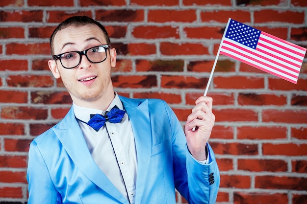 Retrato de un joven (gay) con gafas en un elegante traje y corbata sostiene la bandera de América en sus manos. concepto de desfiles gay en los EE. UU.