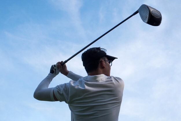 Foto retrato de un joven golfista asiático con un palo de golf en el fondo del cielo azul