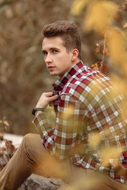 Retrato de joven guapo en camisa a cuadros mirando hacia el lado con el telón de fondo del follaje otoñal