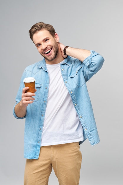 Retrato de joven guapo en camisa de jeans sobre pared ligera sosteniendo una taza de café para llevar