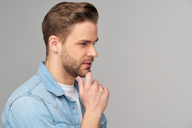 Retrato de joven guapo en camisa de jeans sobre pared ligera