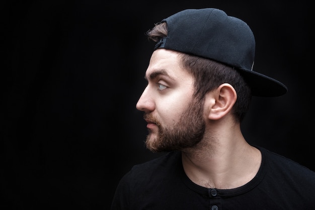 Retrato de joven guapo con camisa negra y gorra sobre fondo negro rapero