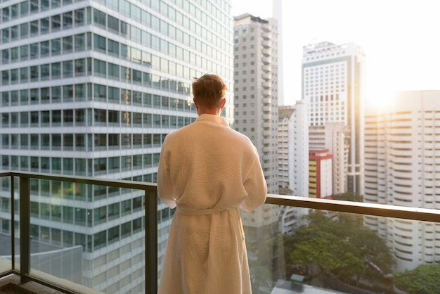 Retrato de joven guapo disfrutando de la vista de la ciudad desde el balcón