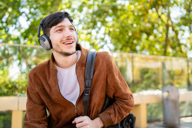 Retrato de joven guapo escuchando música con auriculares mientras está sentado al aire libre. Concepto urbano.