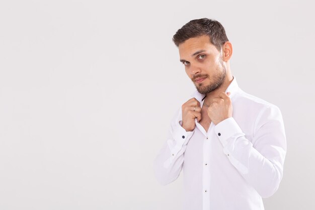 Retrato de joven guapo feliz en camisa casual de pie contra la pared blanca con espacio de copia